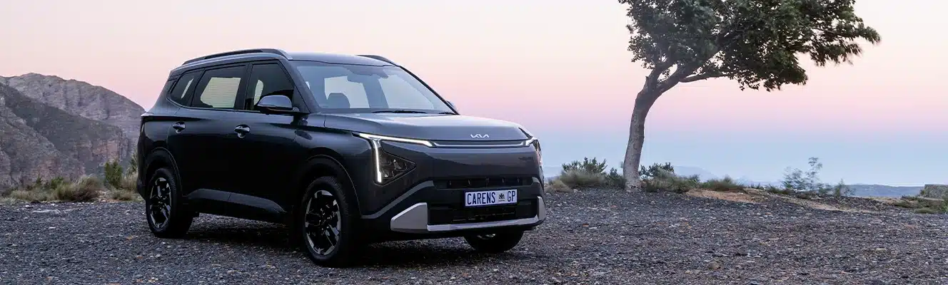 Kia Carens parked beside a tree with mountains in the distance