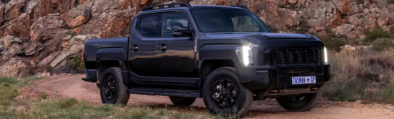 Dark Kia Tasman beside a rocky mountain landscape